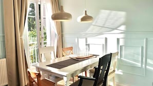 Comedor con una mesa blanca, dos lámparas colgantes y vistas al exterior con vegetación.