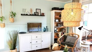 Una sala de estar con televisor, muebles de mimbre, una estantería y una lámpara colgante.