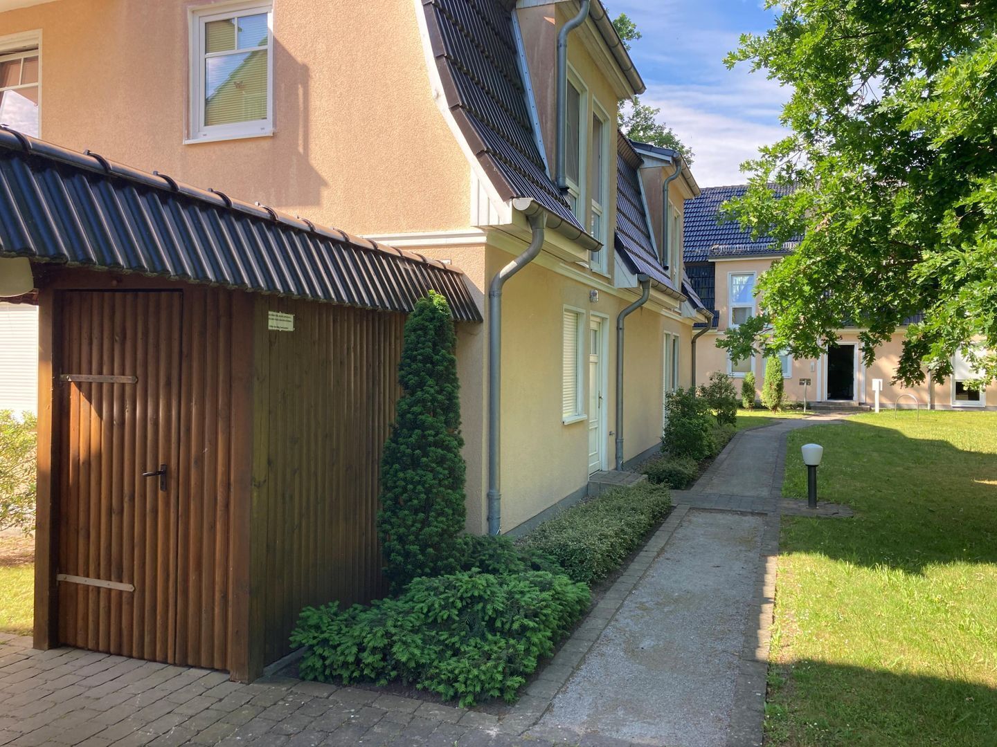 A residential building with a wooden garage door, a small garden, and a pathway leading to the entrance.