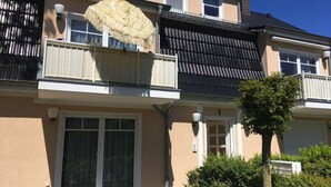 Un edificio residencial de dos pisos con un balcón, un ventanal grande y una puerta.