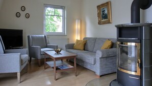 Una sala de estar con sofá, sillón, mesa de centro, televisor y estufa de leña.