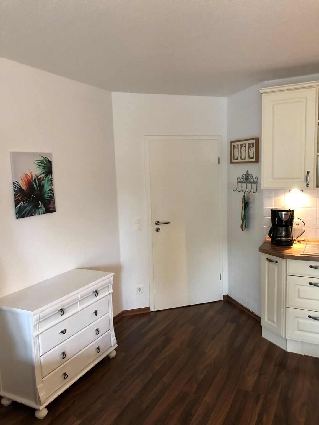 A small kitchen with a white cabinet, a white dresser, and a coffee maker on the counter.