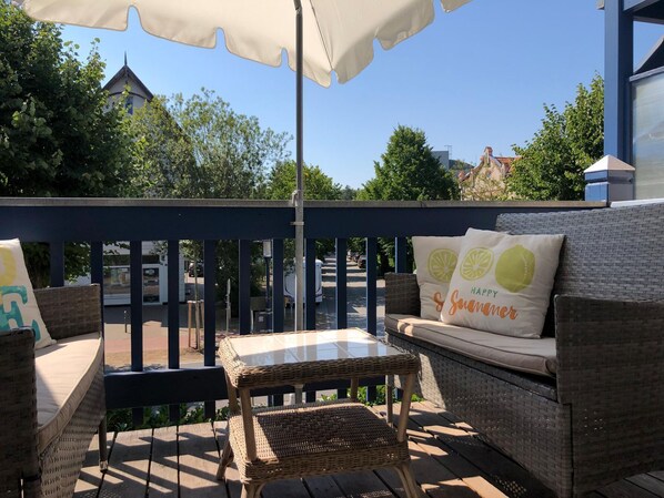 A patio with wicker furniture, a glass table, and a white umbrella.