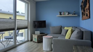 A modern living room with a grey sofa, a coffee table, a TV, and a bookshelf. - Apartment KWi 59 OG - 2-room apartment for 2 pers. with WLAN (Gelbensande)