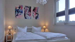 A double bed with white bedding, two bedside lamps, and abstract art on the wall. - Apartment KWi 59 OG - 2-room apartment for 2 pers. with WLAN (Gelbensande)