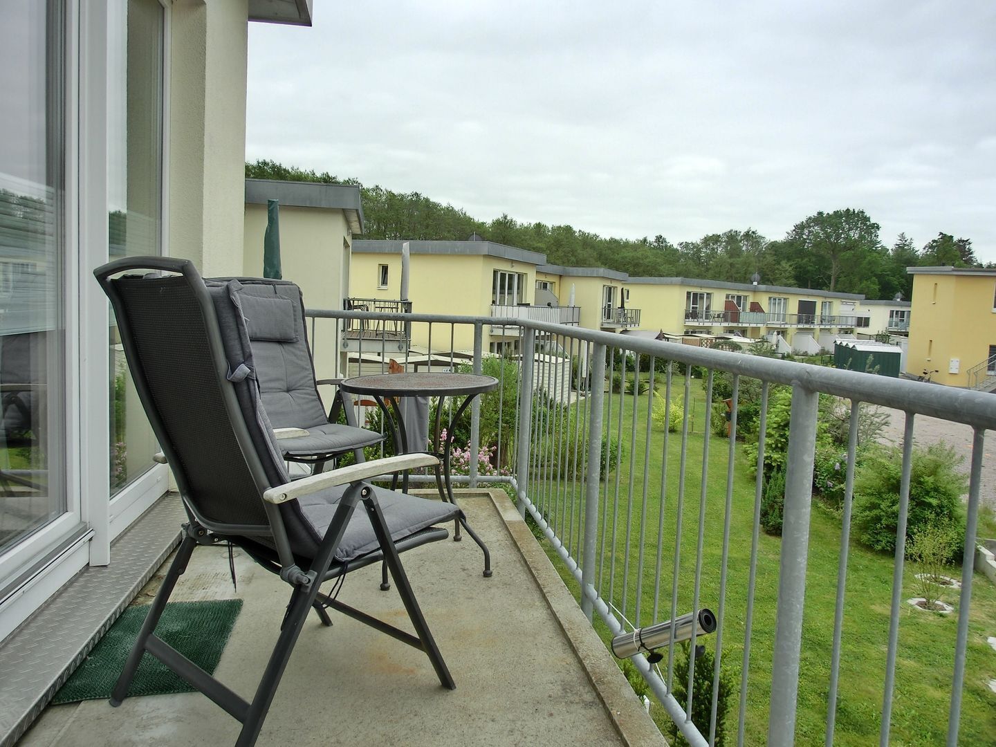 Een balkon met een stoel en tafel, met uitzicht op een woonwijk met huizen en groen.