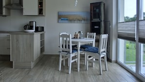 A modern kitchen with a dining area, featuring a white table and chairs, a painting on the wall, and a view through the window. - Apartment KWi 59 OG - 2-room apartment for 2 pers. with WLAN (Gelbensande)