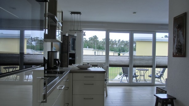 A modern kitchen with a large island, a dining area with a table and chairs, and a balcony with a view of the surrounding area. - Apartment KWi 59 OG - 2-room apartment for 2 pers. with WLAN (Gelbensande)