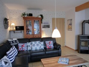 A living room with a black leather sofa, patterned cushions, a wooden cabinet, a hanging lamp, and a fireplace.