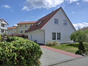 A single-story house with a red-tiled roof, a small porch, and a paved driveway leading to the entrance.