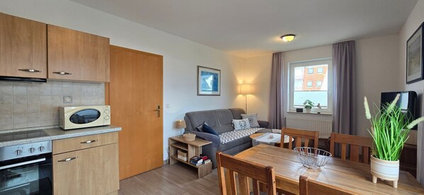 A compact living space with a kitchenette, a sofa, a dining table, and a window with curtains.