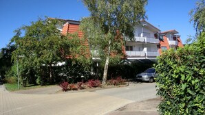 Una strada residenziale con marciapiede lastricato, un'auto parcheggiata e case con tetti rossi e balconi.