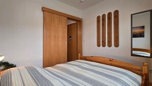 Una camera da letto con un letto, una porta in legno, uno specchio a muro e un comodino con una lampada.