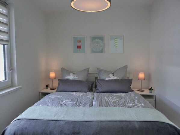 A bedroom with a bed, two bedside lamps, a window, and three wall art pieces.