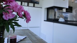 A modern kitchen with a black countertop, a kettle, and a window with a view of the sea.