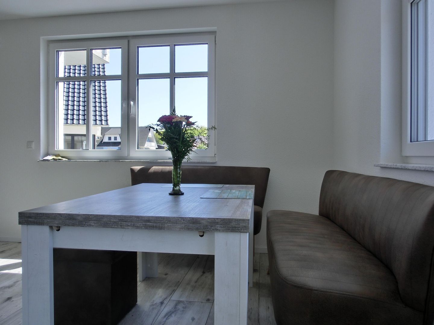 A dining area with a table and chairs, a vase with flowers, and a window with a view of buildings.