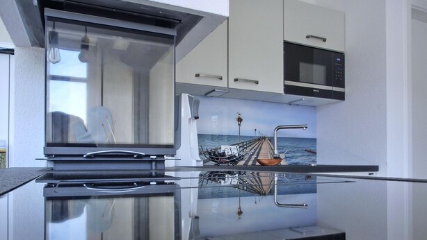 A modern kitchen with a reflective backsplash, stainless steel appliances, and a view of a boat on the water through the window.