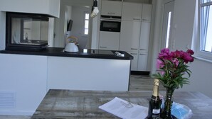 A modern kitchen with white cabinets, a black countertop, and a kettle. There's a vase with flowers on the table.