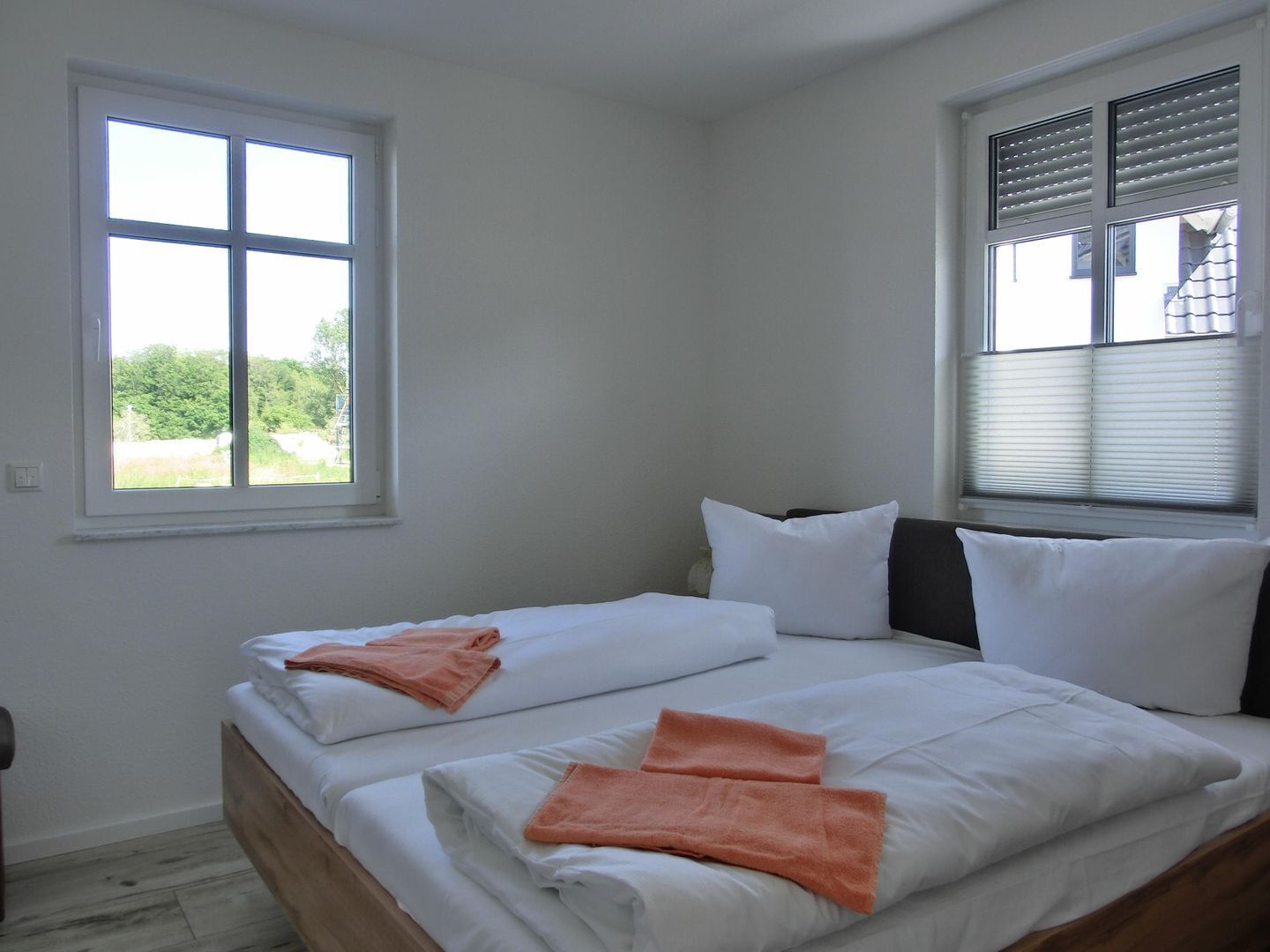 Une chambre avec deux lits, du linge de lit blanc et une fenêtre avec des stores.