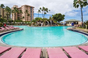 Ein Swimmingpool mit Liegestühlen, Palmen und einem Wasserfall.