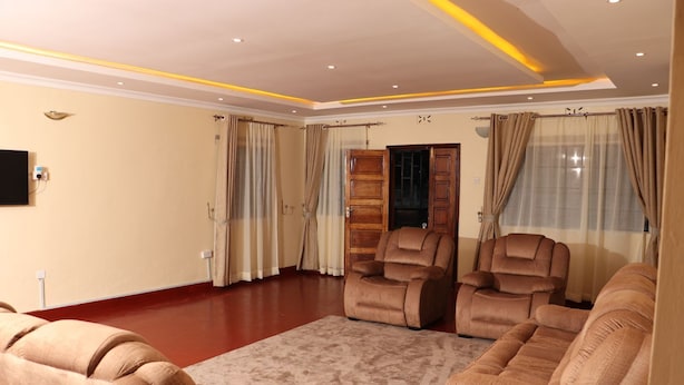 Un vaste salon doté d’un sol rouge, de murs de couleur beige et d’un grand tapis beige. On y trouve trois canapés beiges et deux fauteuils inclinables.