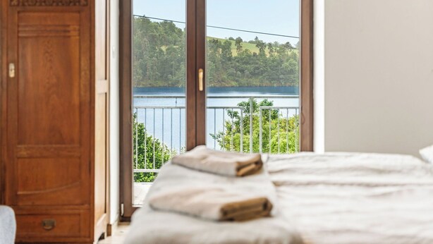 Un dormitorio con un ventanal que da a un lago y un bosque.
