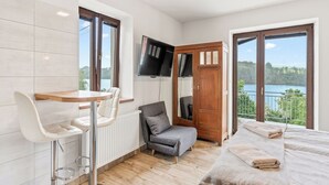 Una habitación con cama, televisión, silla, mesa y ventanas amplias con vista a un lago.