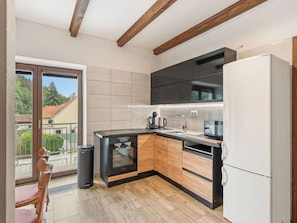 A modern kitchen with a built-in oven, a refrigerator, and a window overlooking a residential area. - Cosy apartment for 9 people with WIFI, pool, TV, patio and pets allowed (Příbram)
