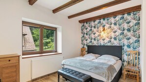 Une chambre à coucher avec un lit, un banc, des meubles en bois, une fenêtre et un radiateur.