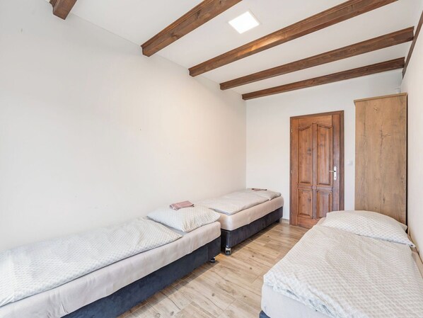 A bedroom with two single beds, wooden beams on the ceiling, a wardrobe, and a door.