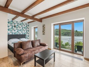 Ein Schlafzimmer mit einem Bett, einem braunen Sofa, einem kleinen Tisch, einem Balkon mit Seeblick und einem Wandpapier mit Muster.