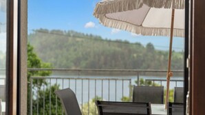 Un balcón con vista a un lago y colinas, una silla y una sombrilla.