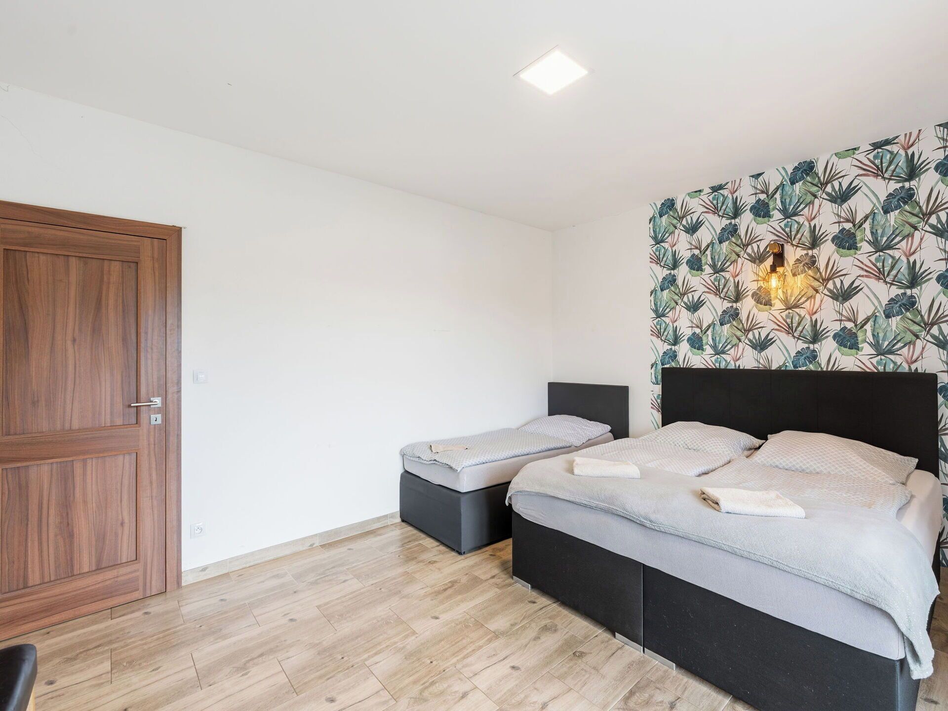 A bedroom with two beds, a wooden door, and a wall with a tropical leaf pattern.