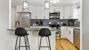 A modern kitchen with white cabinets, a black and white tiled backsplash, stainless steel appliances, and two black bar stools. - Cozy newly remodeled home close to major amenities  in Connecticut a (Middletown)