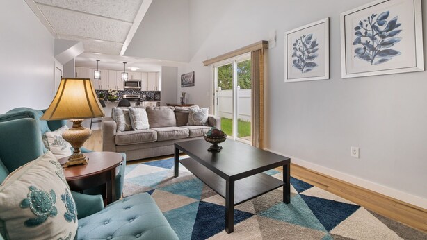 A living room with a sofa, armchair, coffee table, and lamp. There is a kitchen in the background, and the room has a large window. - Cozy newly remodeled home close to major amenities  in Connecticut a (Middletown)