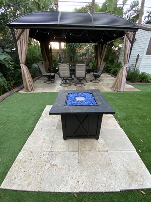 A patio area with a fire pit table, outdoor seating, and a covered gazebo.