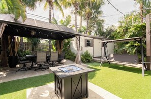 A covered patio area with a table and chairs, a fire pit, and a swing set.
