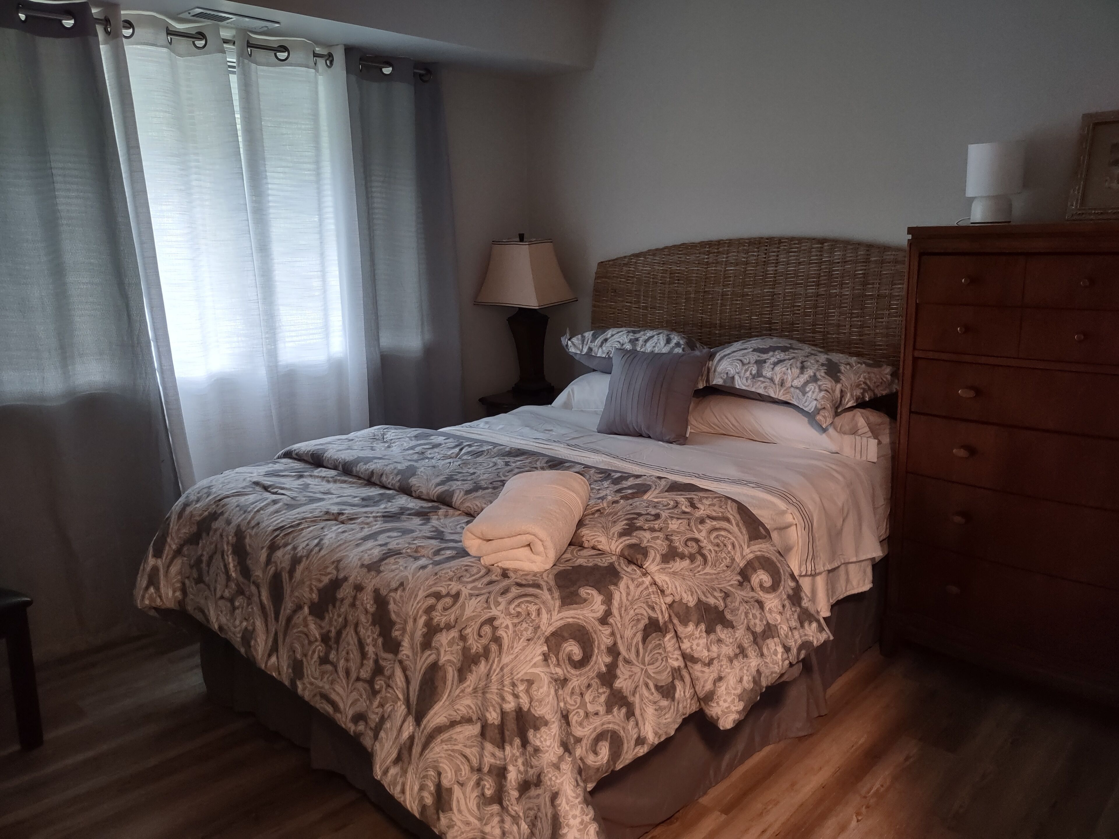 A bedroom with a bed, a dresser, a lamp, and a window with curtains.