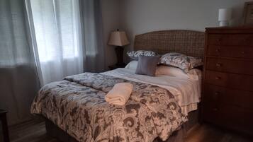 A bedroom with a bed, a dresser, a lamp, and a window with curtains.