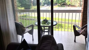 A balcony with wicker furniture and a small table with flowers, overlooking a green lawn and a parking area. - Idyllic Central Raleigh condo-3br/2bath (Raleigh)
