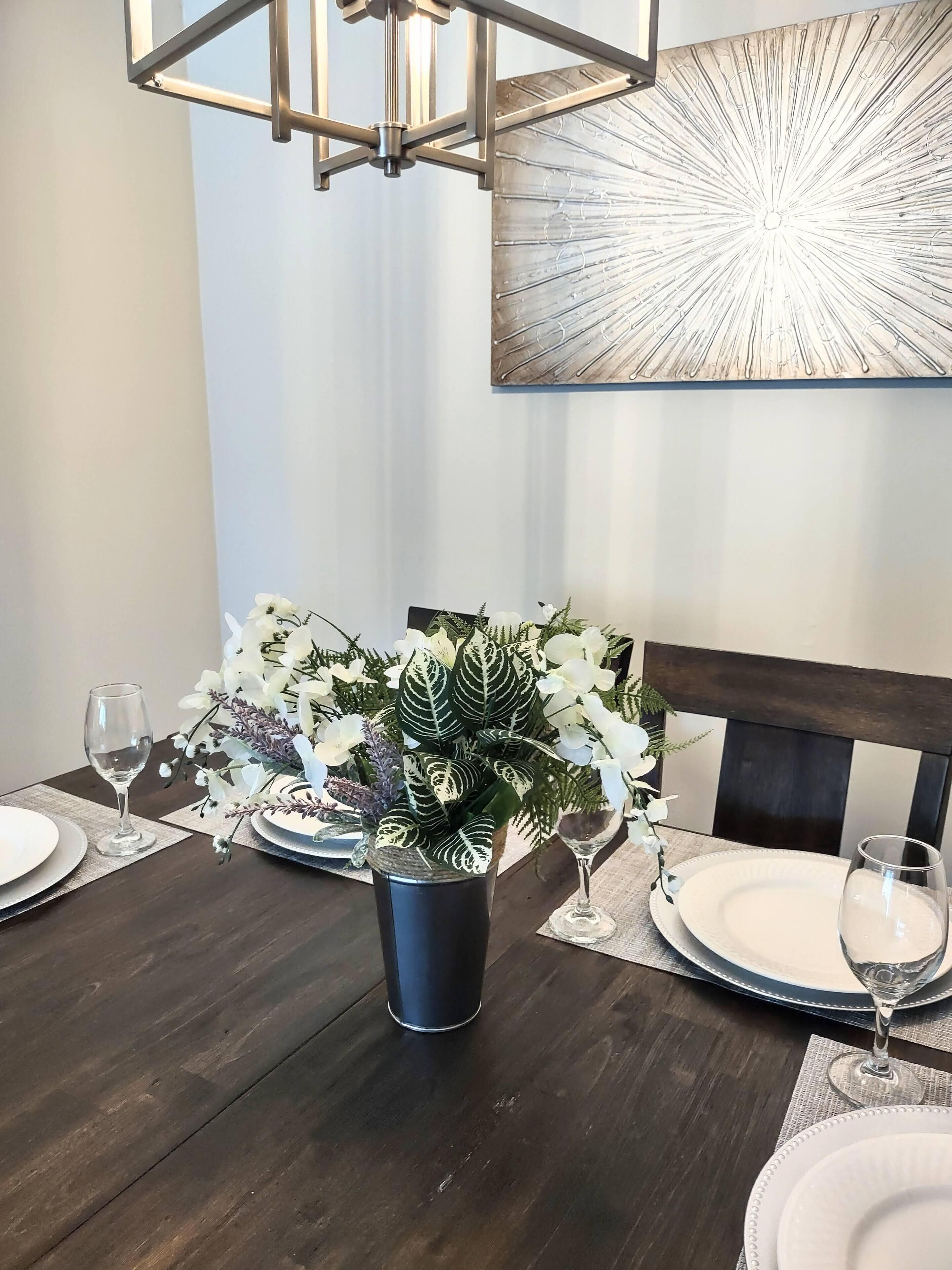 A dining table set with plates, glasses, and a centerpiece of white flowers and green foliage.
