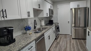 A modern kitchen with white cabinets, stainless steel appliances, a granite countertop, and a wooden floor. - Idyllic Central Raleigh condo-3br/2bath (Raleigh)
