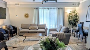 A living room with a sofa, coffee table, dining table, and chairs. There is a plant on the dining table. - Idyllic Central Raleigh condo-3br/2bath (Raleigh)