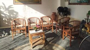 Een kamer met houten stoelen rondom een kleine tafel, een schilderij aan de muur en een plant in een pot.