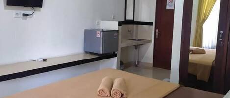Una habitación de hotel con cama, escritorio con ordenador, televisión y espejo.