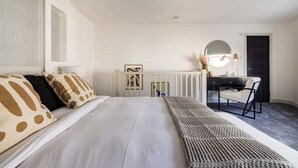 Een slaapkamer met een groot bed, een bureau met stoel, een ronde spiegel en een radiator.