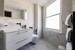 A modern bathroom with a white vanity, a toilet, and a large window. - The Battersea Secret - Modish and Bright 1bdr Flat (London)