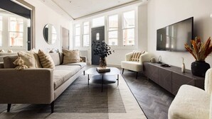 Een moderne woonkamer met een bank, fauteuils, een salontafel en een televisie.