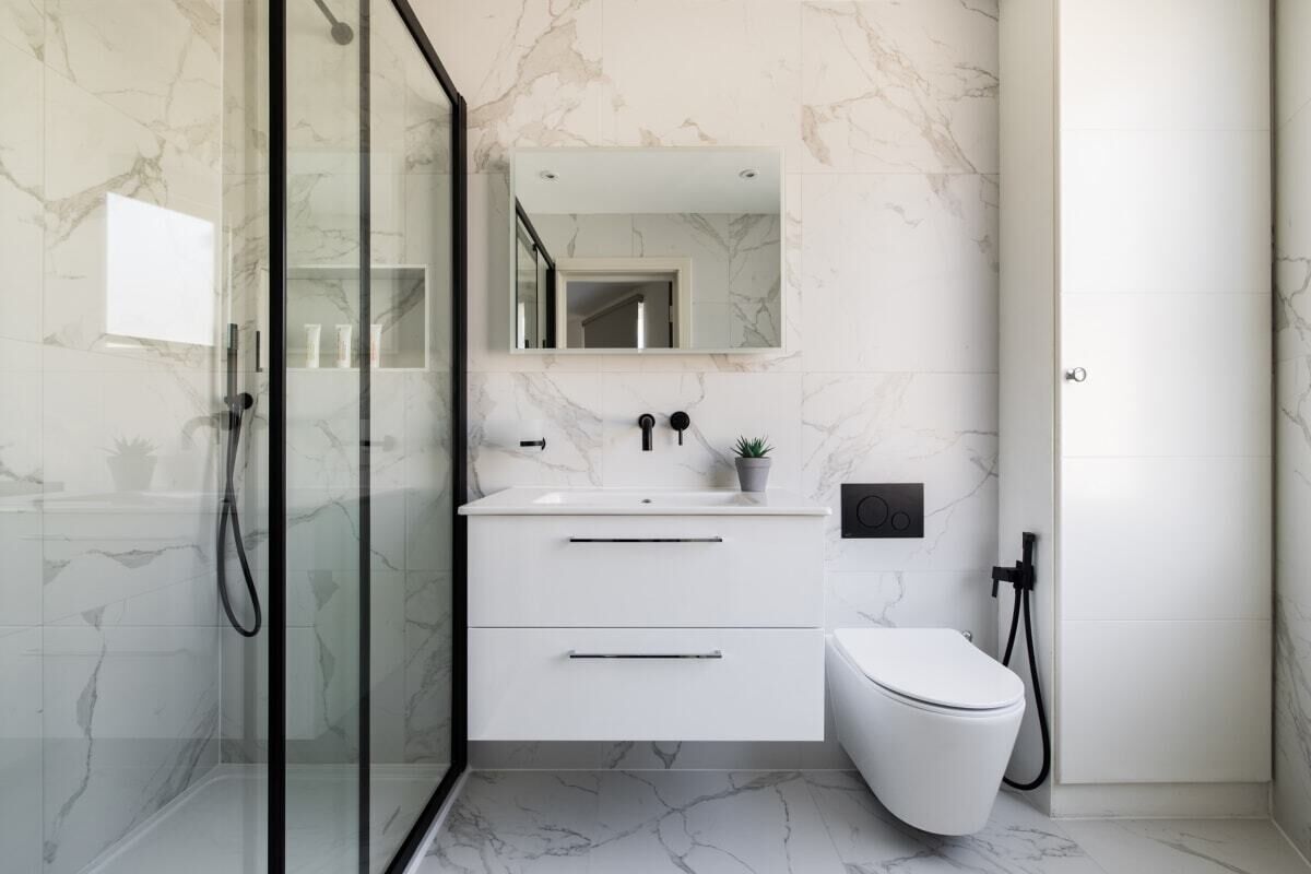 A modern bathroom with a glass shower enclosure, a white sink with a marble countertop, a toilet, and a mirror above the sink.