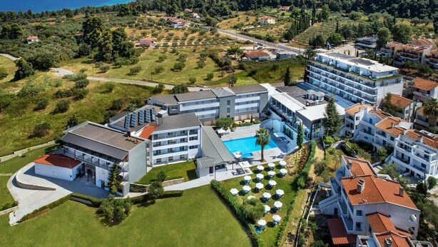 A modern hotel with multiple buildings, a swimming pool, and a view of the sea.